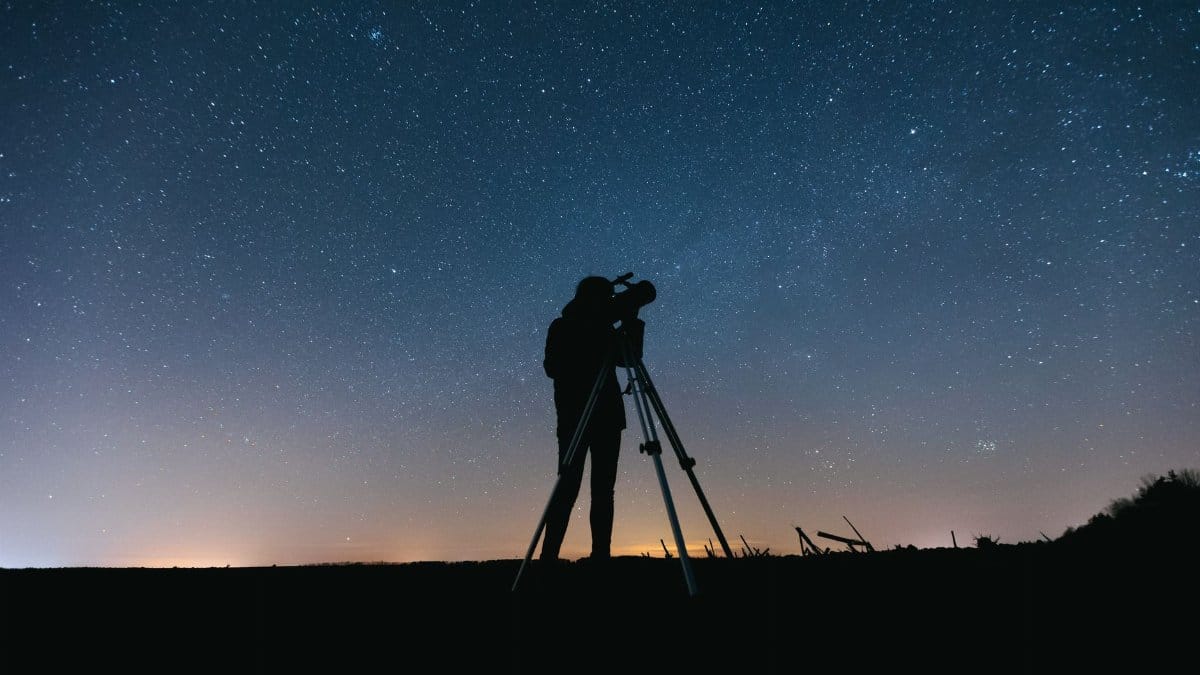 Silhouette of a person using a telescope under a starry night sky, perfect for astronomy themes.