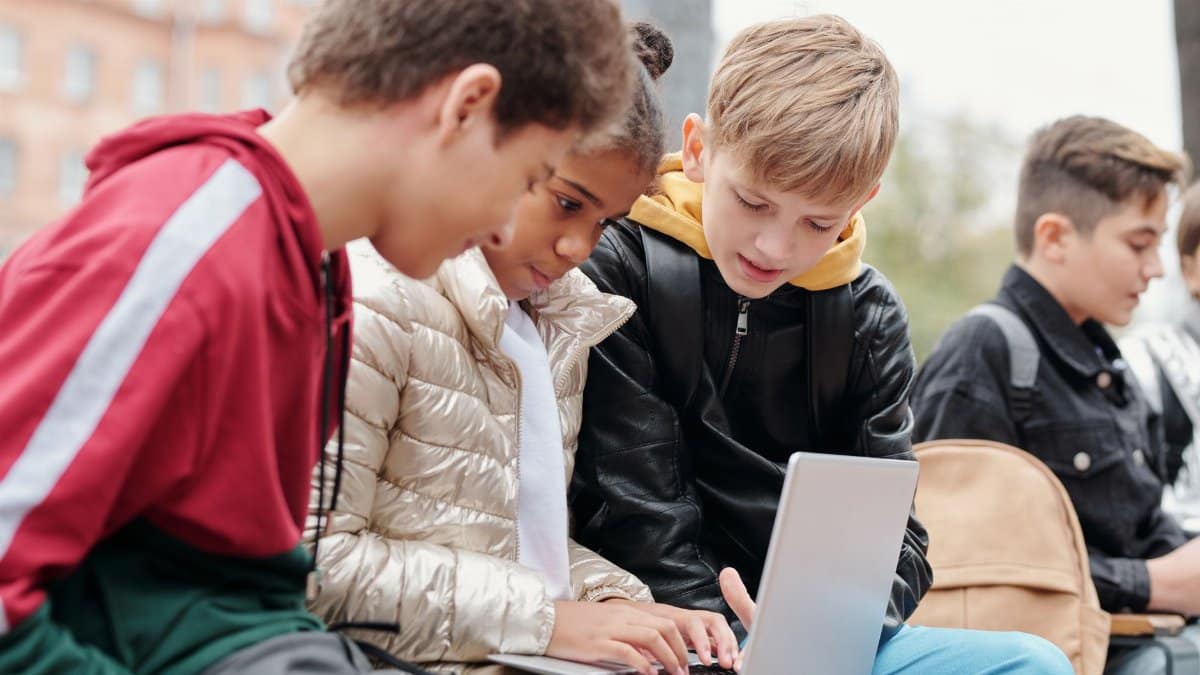 Group of teenagers studying together on a laptop outdoors, fostering collaboration.