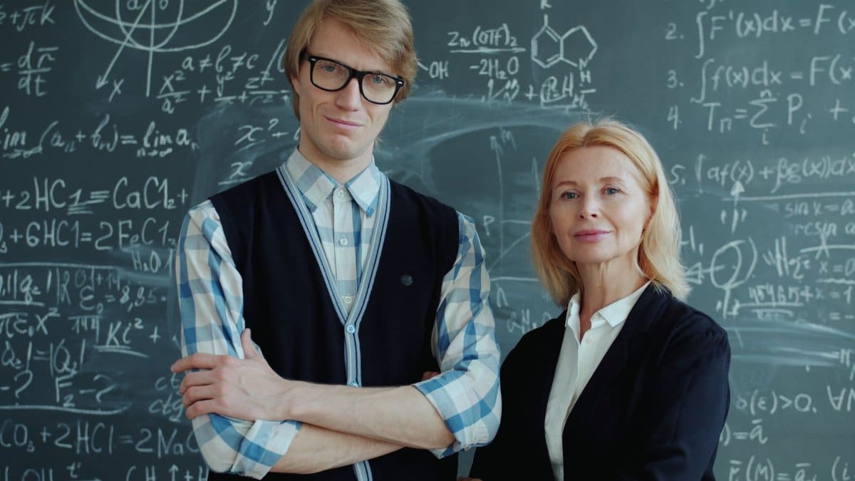 Two educators posing confidently in front of a math-covered blackboard.