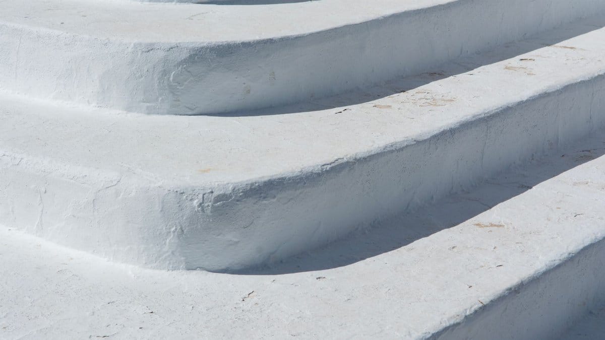 Close-up of textured white concrete steps in bright sunlight, showcasing minimalist design.