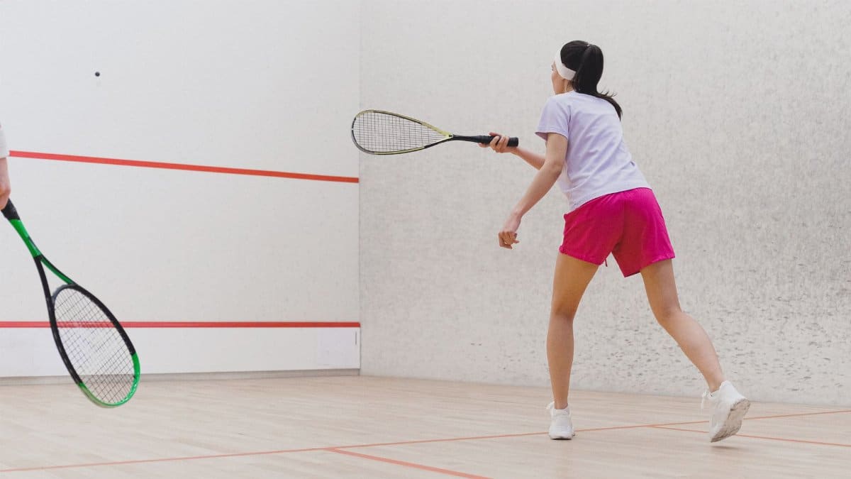 Woman playing squash on an indoor court, focused on the game with racket in hand.