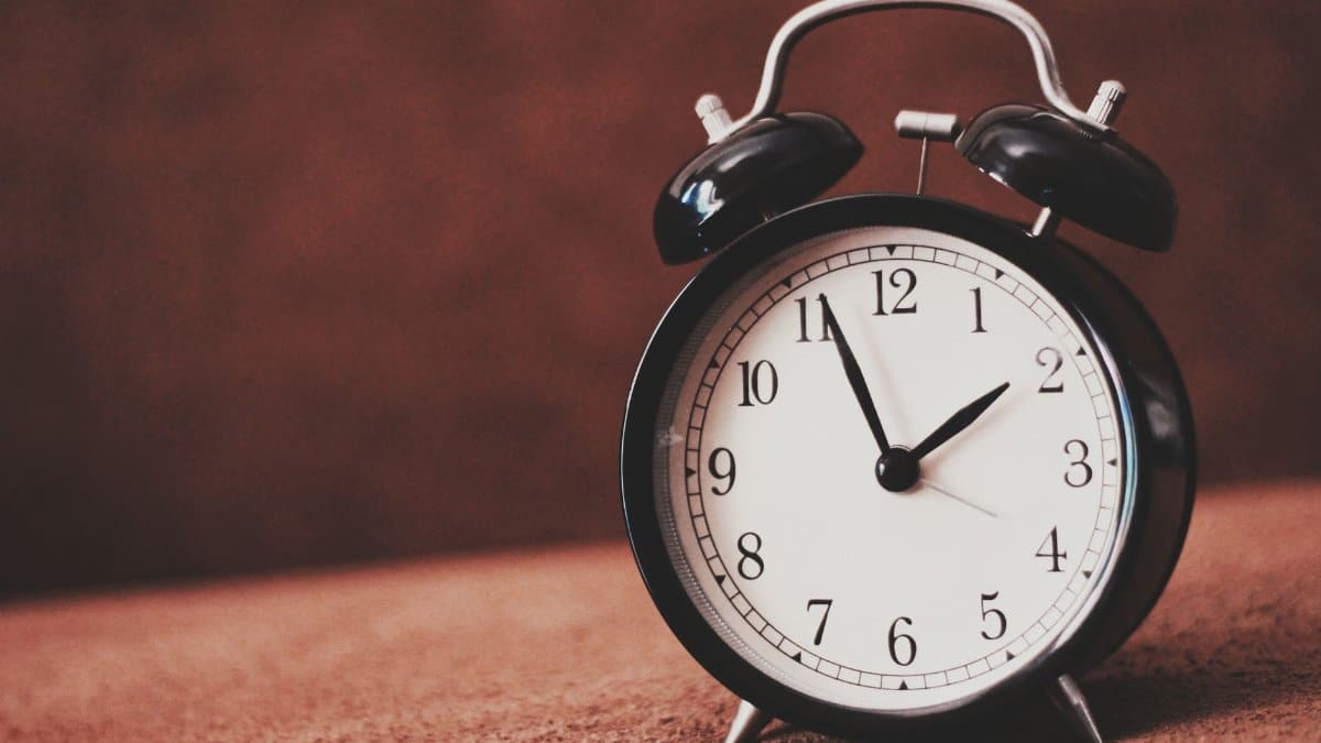 Close-up of a vintage black alarm clock showing twelve o'clock against a brown backdrop.
