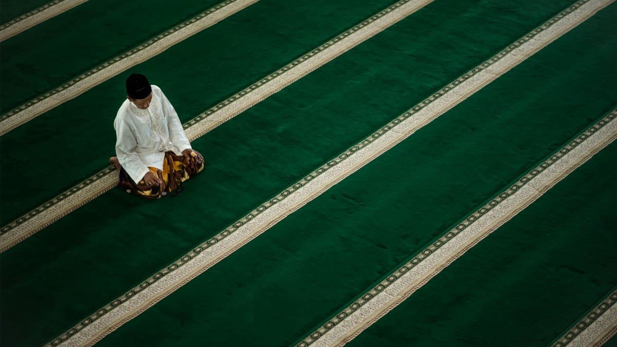A single man prays in a mosque in Aceh, Indonesia, on a green carpet during the day.