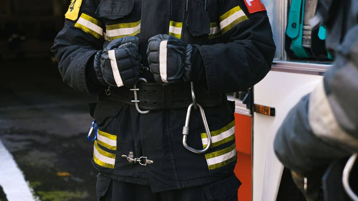 Firefighter in uniform with rescue equipment near emergency vehicle, highlighting safety and readiness.