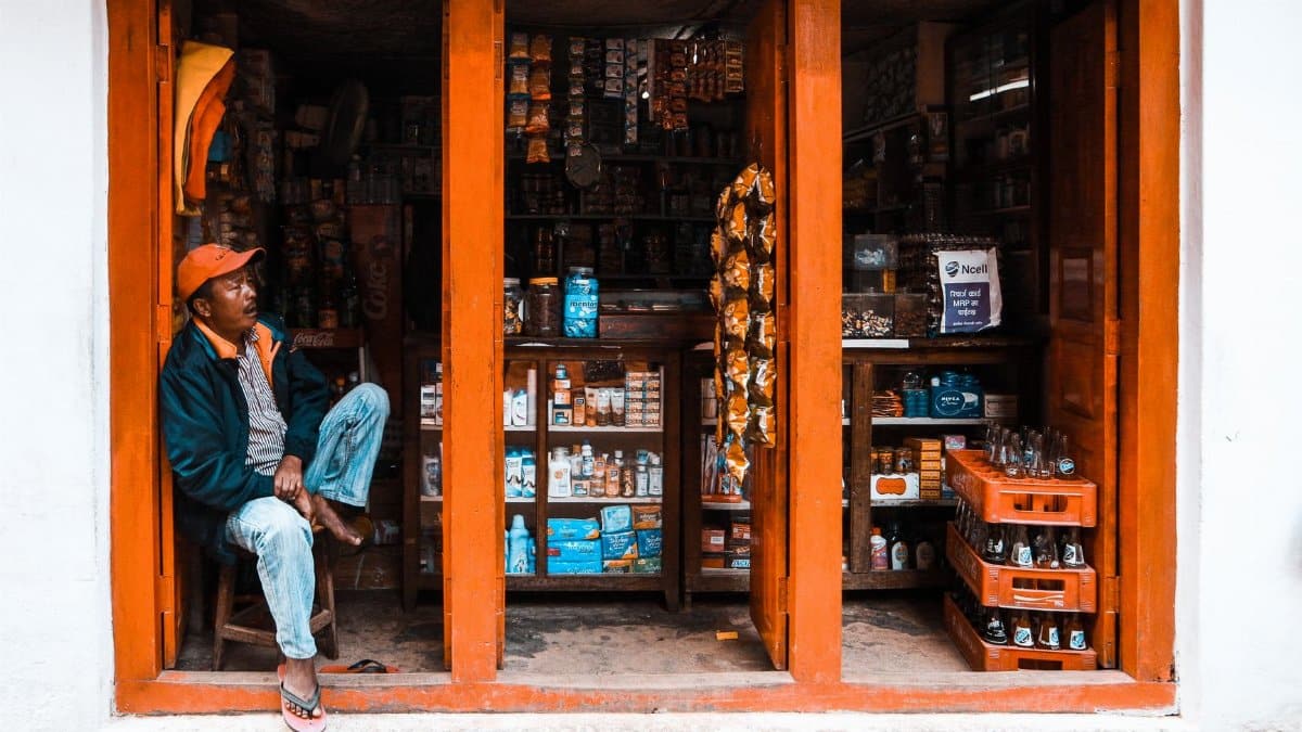 Casually dressed man sitting in doorway of local store with colorful products displayed.