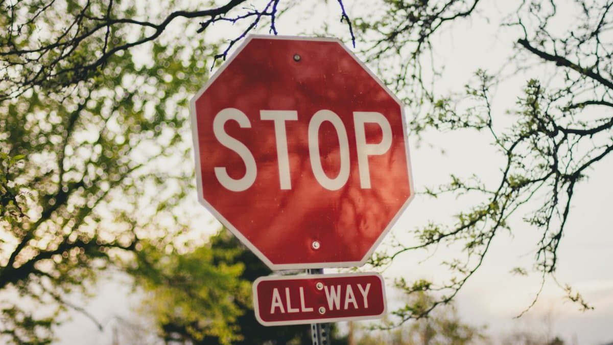 A clear red stop sign with 'All Way' below it in a sunny suburban setting.