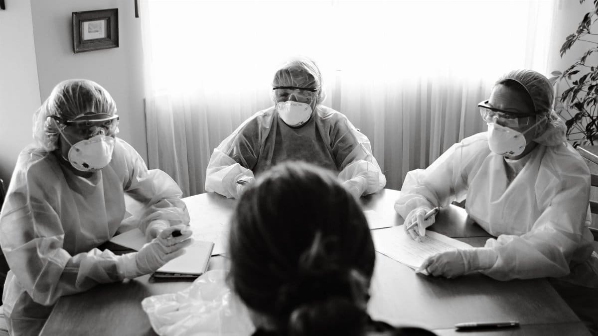 Black and white photo of healthcare team in PPE holding a meeting indoors.