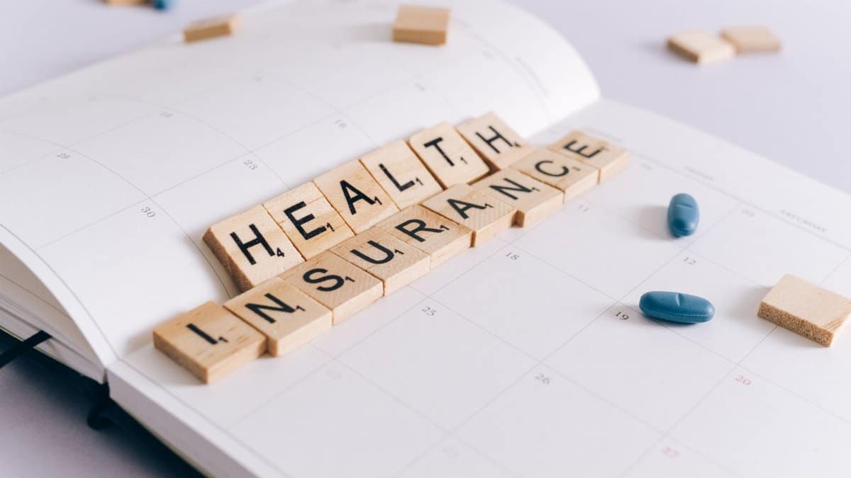 Scrabble tiles spelling 'Health Insurance' on a calendar with pills.