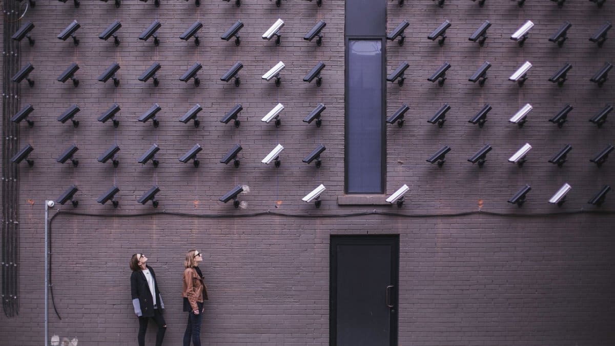 Women observing a wall covered with numerous security cameras in an urban setting, showcasing modern surveillance.