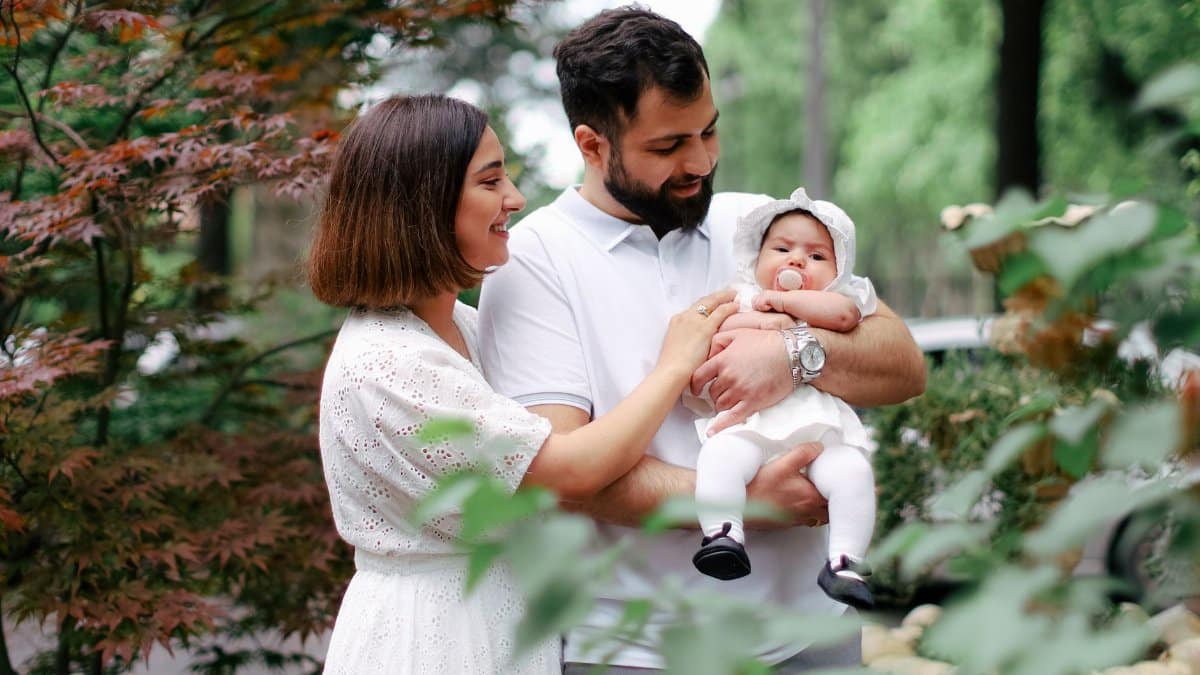 A joyful family moment with parents and their baby in a beautiful green garden.
