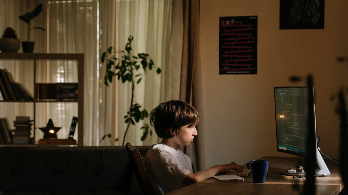 A young boy intensely focused on coding on a computer in a cozy, dimly-lit room.