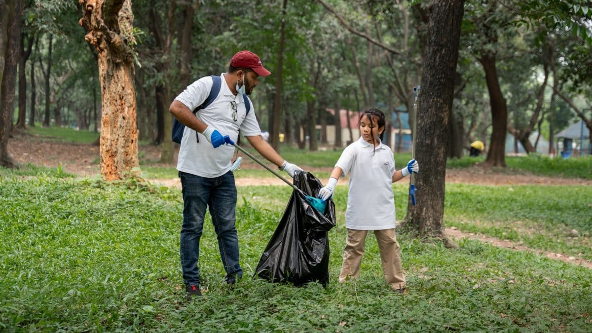 Two volunteers collect litter in a park, promoting environmental awareness and community service.