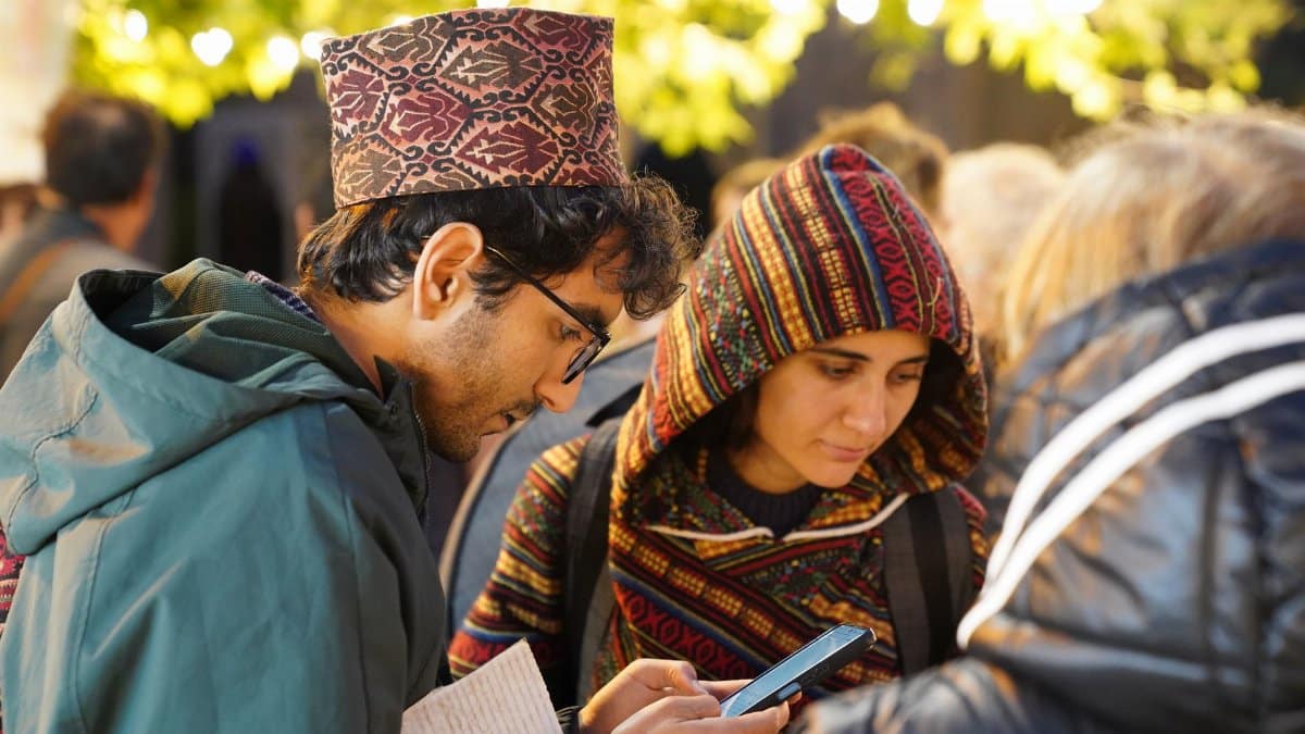 Two adults engaged with a smartphone at an outdoor social event under string lights.