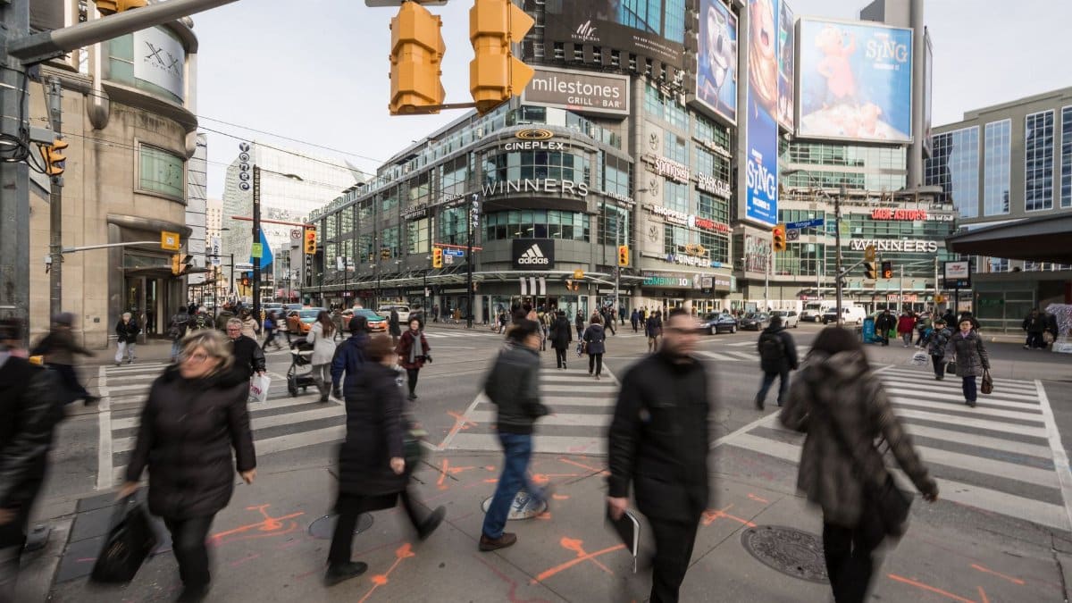 People crossing a busy city intersection with tall buildings and advertisements in daylight.