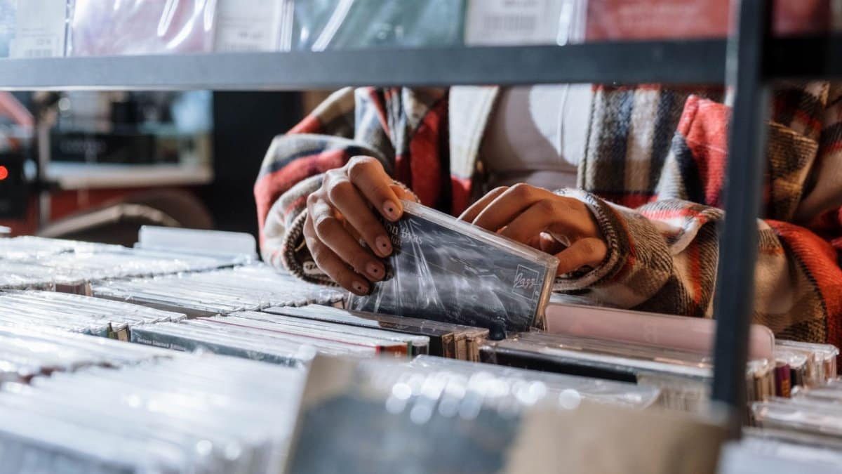 Close-up of hands picking CDs from a record shop shelf, highlighting the tactile music shopping experience.
