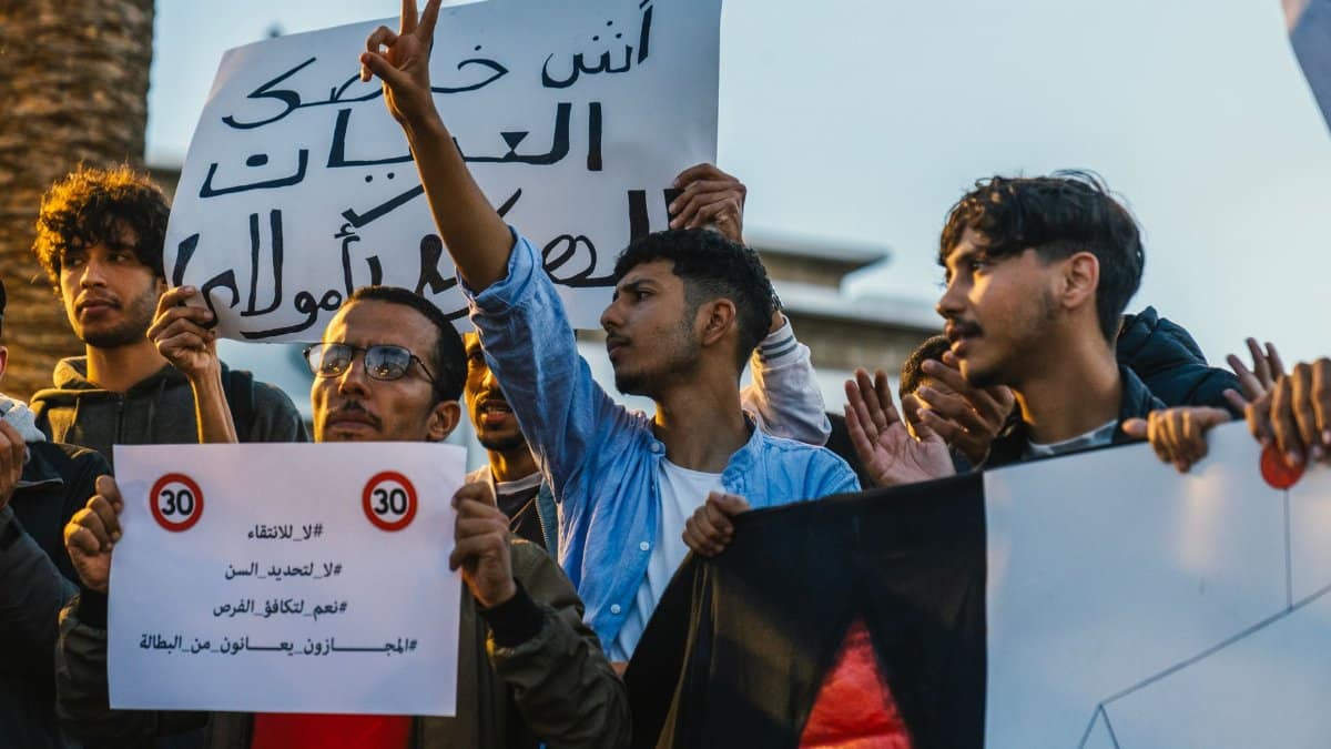 Young adults protest with signs expressing political and social messages outdoors.