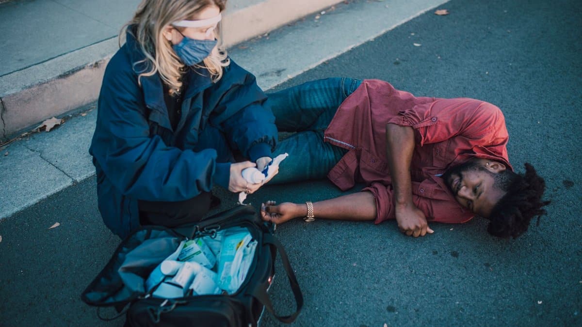 Paramedic provides first aid to injured man lying on roadside.