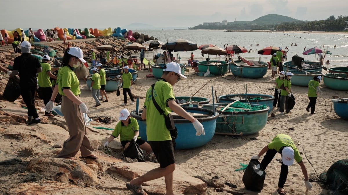 A group of volunteers in green shirts clean up trash on a beach, promoting environmental awareness.