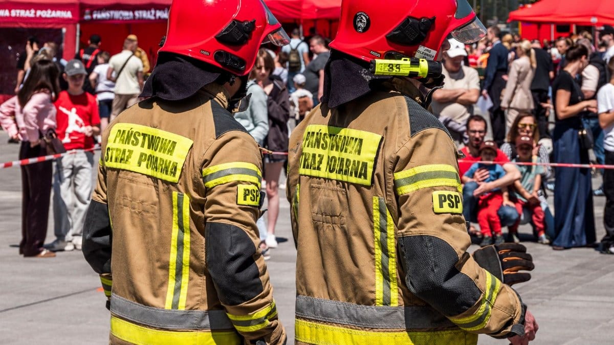 Two Polish firefighters in red helmets at a public safety event outdoors.