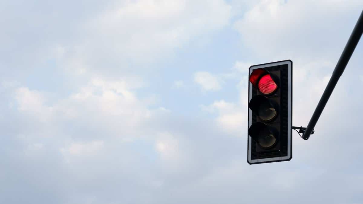 Red traffic light set against a bright, cloudy sky. Perfect for themes of travel, technology, and safety.