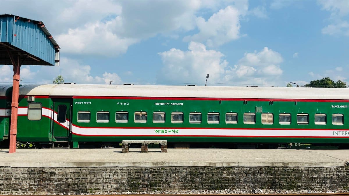 A vibrant green Bangladesh Railway train at a station under a clear sky.