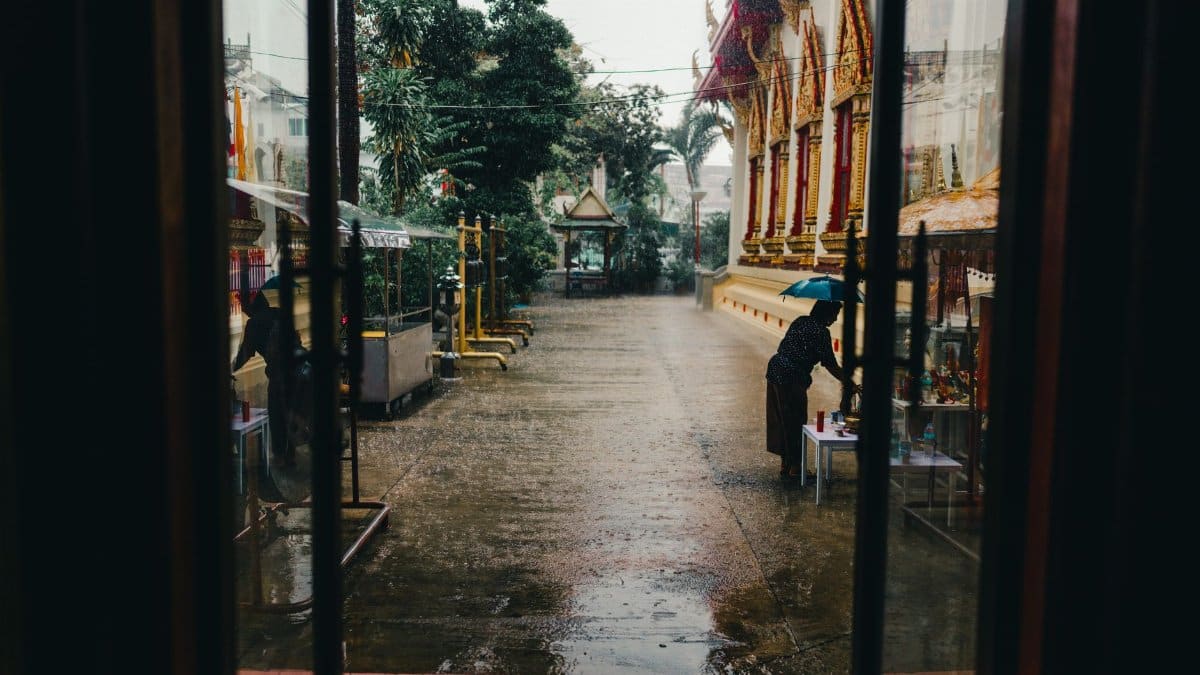 A person under an umbrella near a temple in the rain in Bangkok, Thailand.