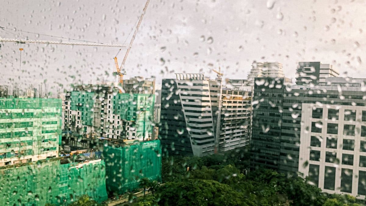 View of modern city buildings seen through a rain-covered window, creating a moody atmosphere.