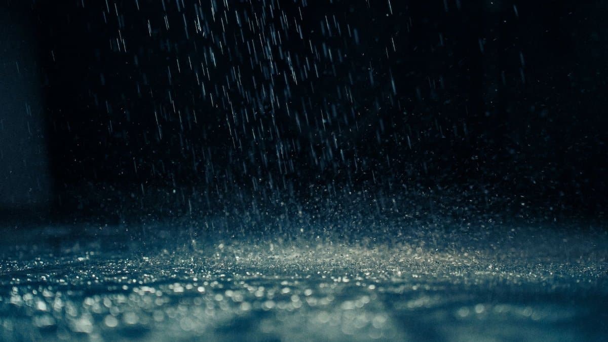 Dramatic close-up of rain droplets falling on a dark surface, capturing movement and reflections.