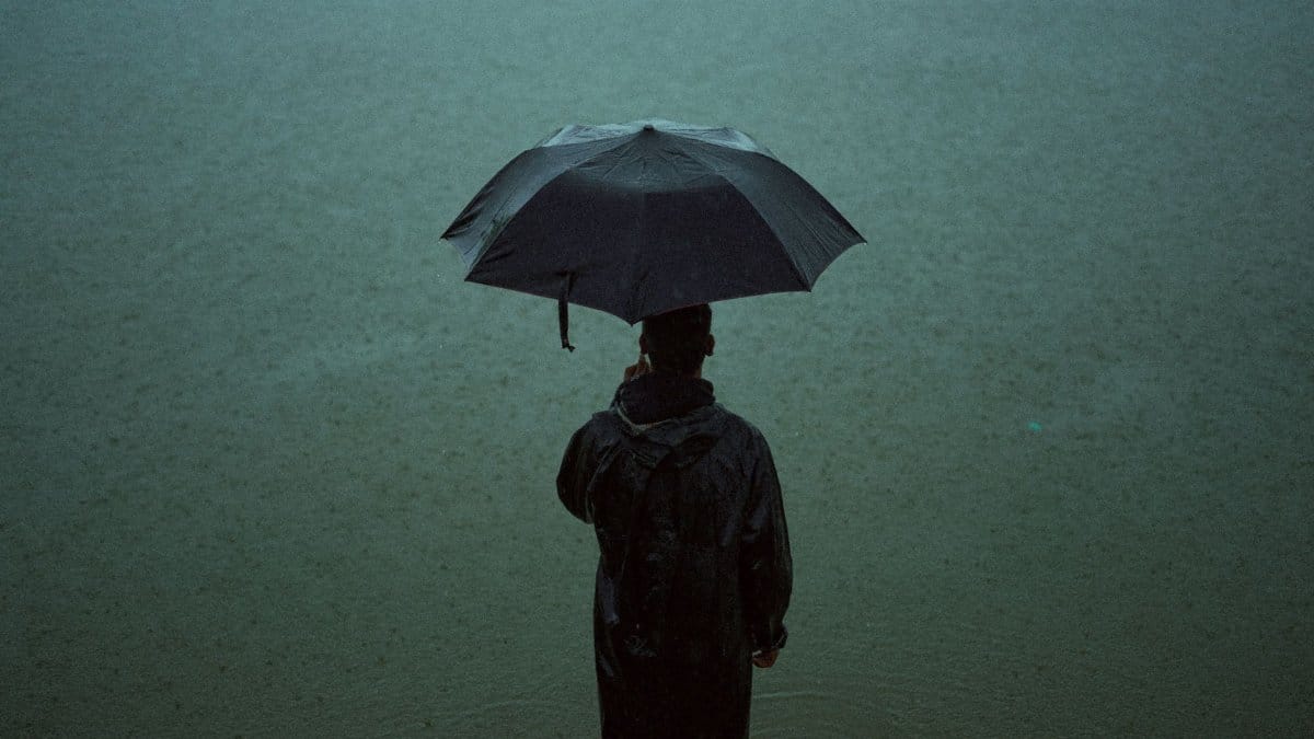 A person stands alone in the rain, holding an umbrella, creating a moody atmosphere.