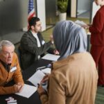 Adults engaging in the voting process at an indoor polling station, representing diverse backgrounds and social responsibility.