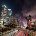 Dynamic night cityscape of Los Angeles with light trails, skyscrapers, and palm trees.