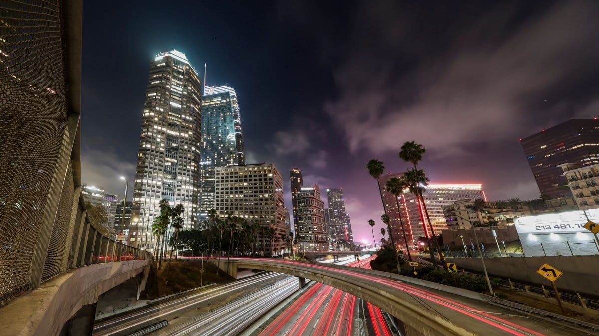 Dynamic night cityscape of Los Angeles with light trails, skyscrapers, and palm trees.