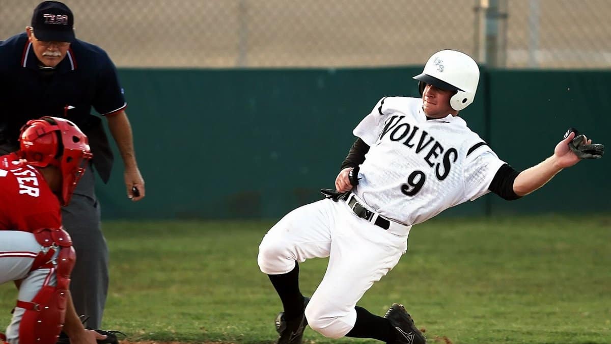 A baseball player wearing a 'wolves' jersey slides into base as the umpire watches intently.
