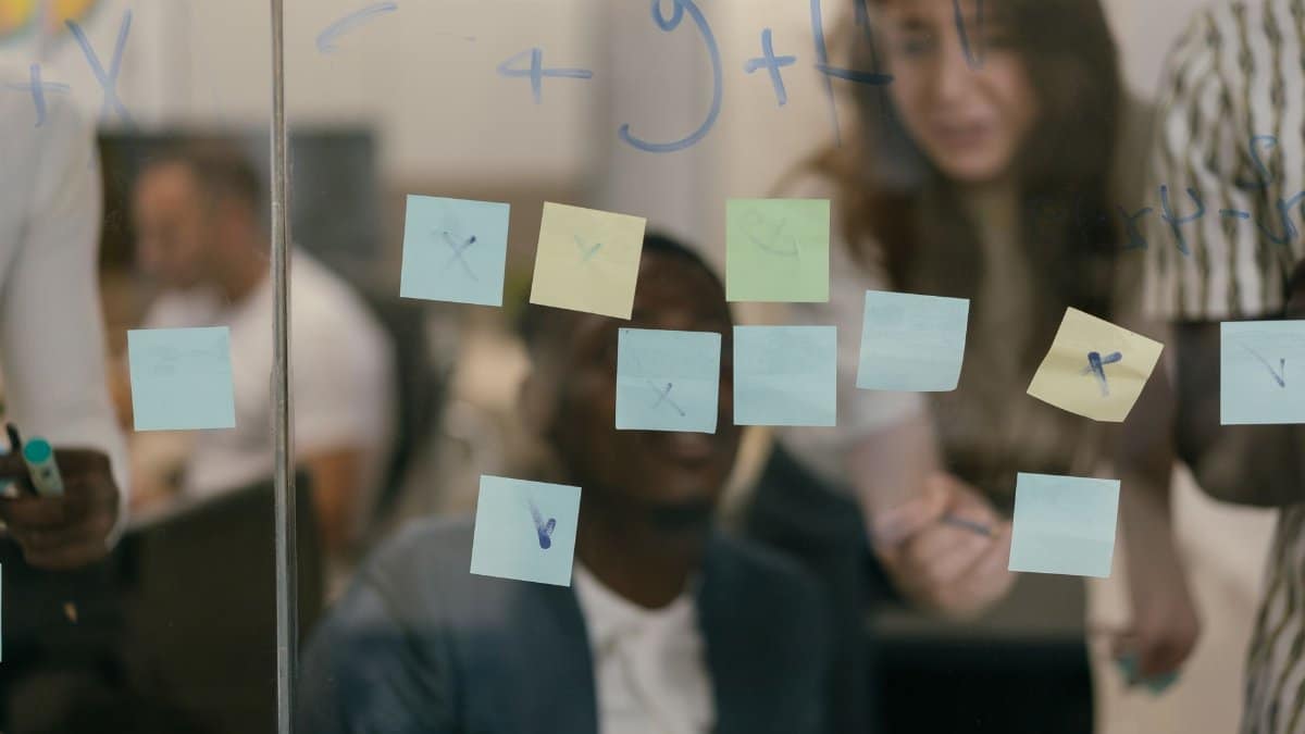 Collaborative meeting with team writing on a glass board covered in colorful sticky notes.