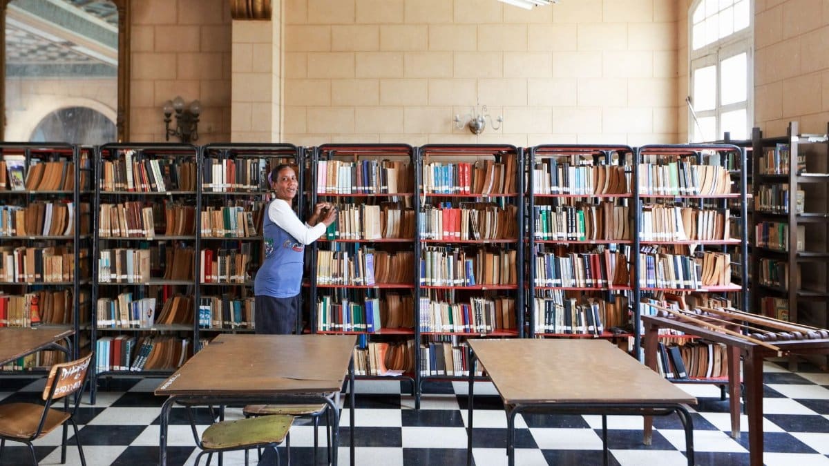 A librarian organizing books in a spacious, classic library with checkered flooring.