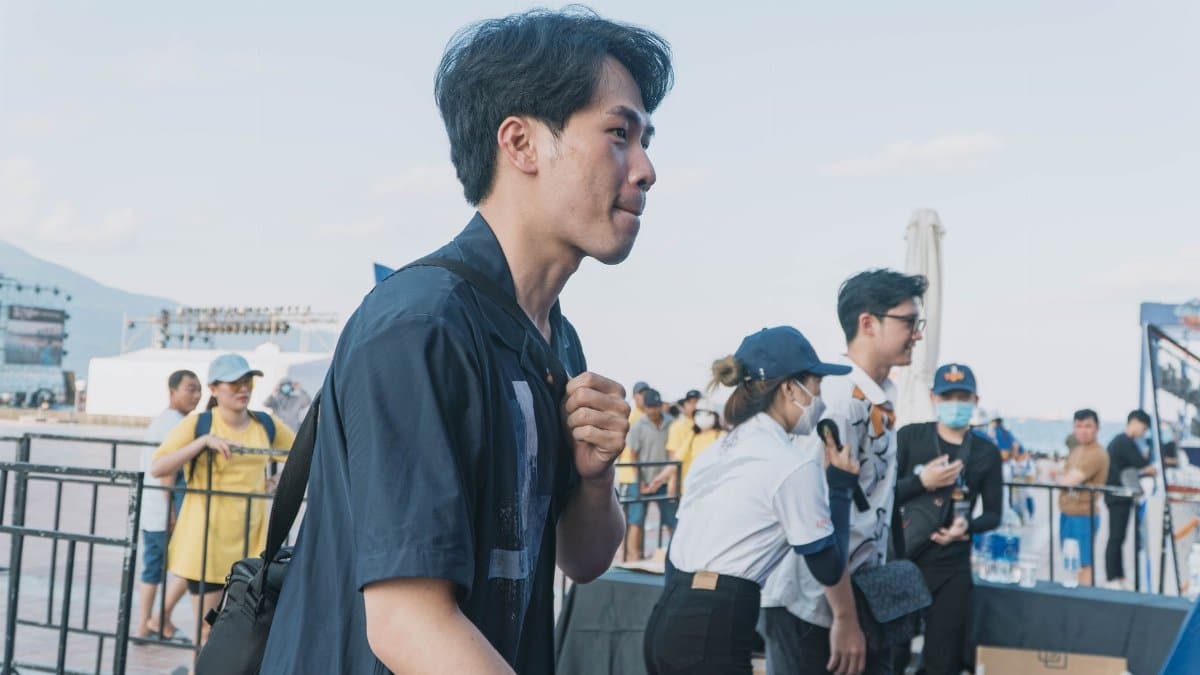 Asian man walking outdoors at a casual event with others nearby.