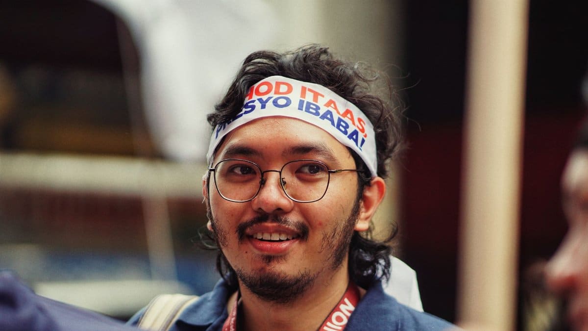 Man wearing glasses and headband at an outdoor event, smiling.