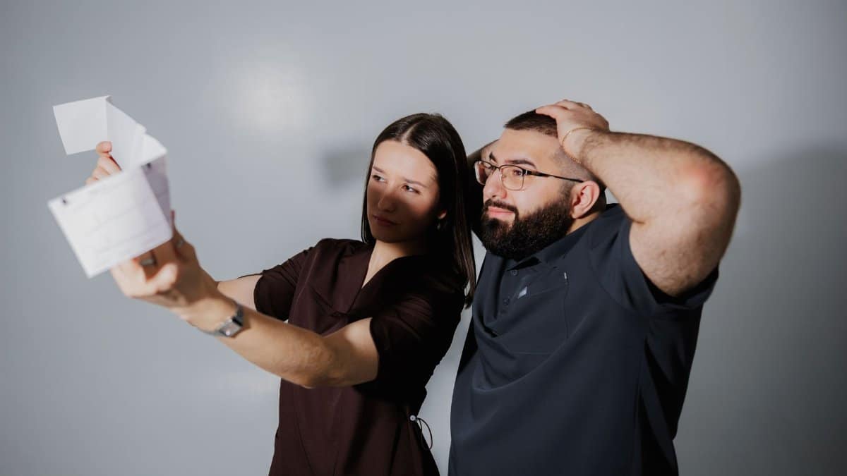 A man and woman react surprisedly while examining a document in a neutral setting.