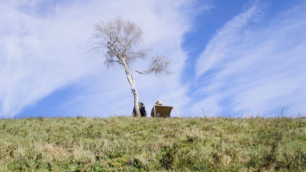 A lone artist paints in the serene landscape of Great Malvern, England, under a clear blue sky.