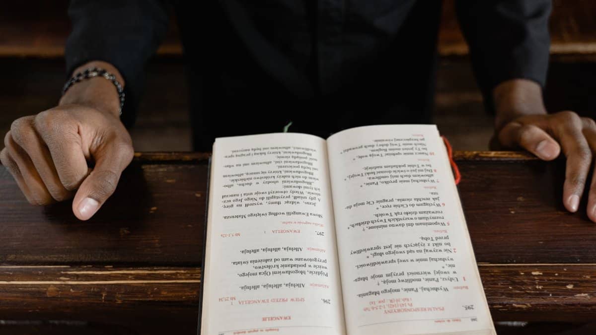 A close-up view of a priest reading an open bible during a church service, focus on hands and book.