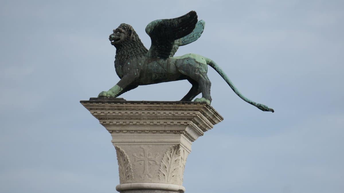 Iconic winged lion statue atop a column in Venice, Italy, against a cloudy sky.