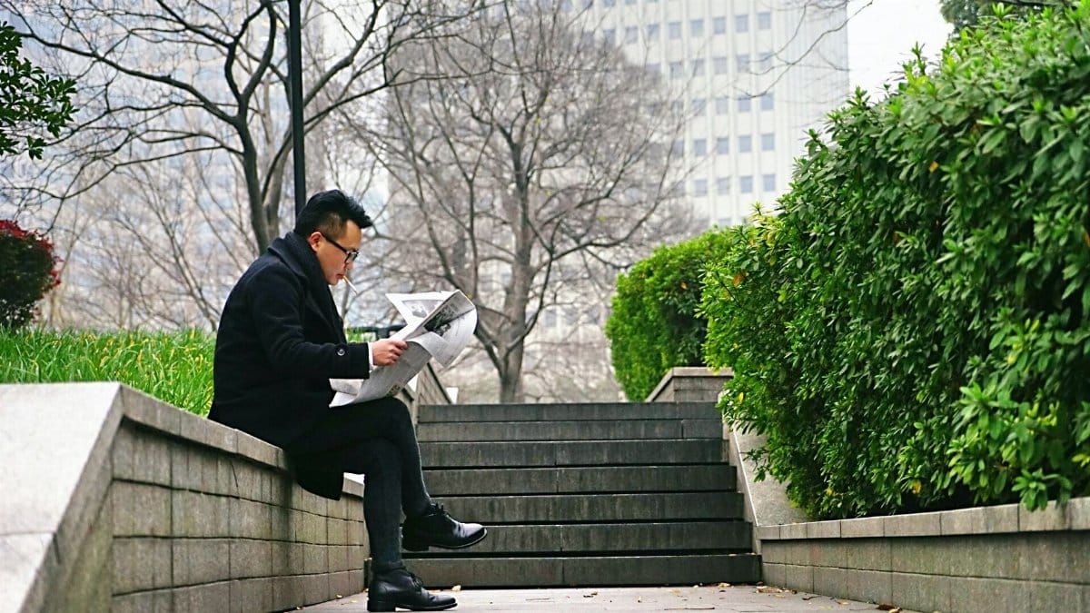 Man reading newspaper outdoors on a park bench during a peaceful afternoon break.