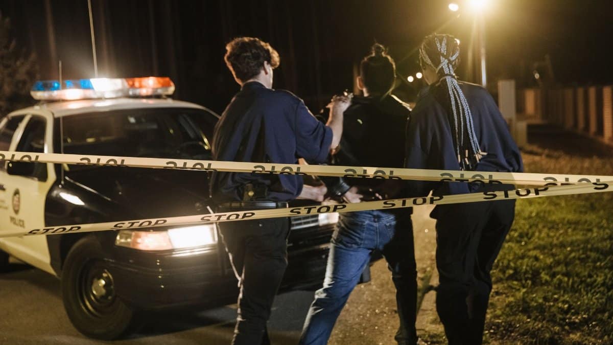 Nighttime arrest scene with police officers and patrol car behind caution tape.