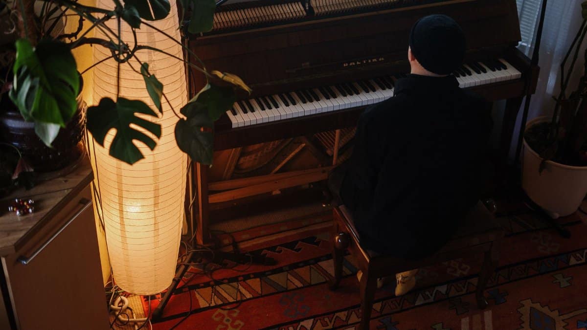 A cozy home interior featuring an upright piano, warm lighting, and a musician seated at the keyboard.