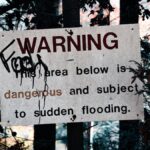 A warning sign about sudden flooding amid a forest setting, emphasizing caution.