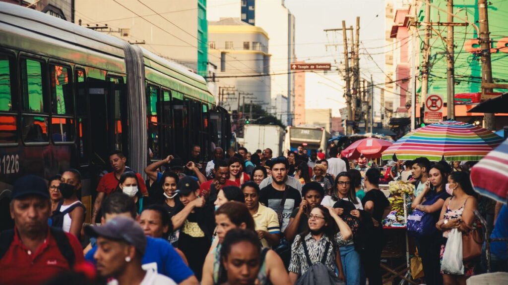 Busy urban street market featuring diverse crowd and public transportation.