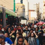 Busy urban street market featuring diverse crowd and public transportation.