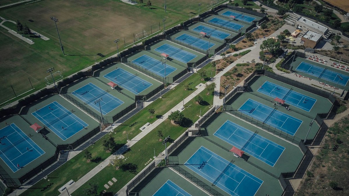 Aerial shot of numerous tennis courts in a recreational park during the day.