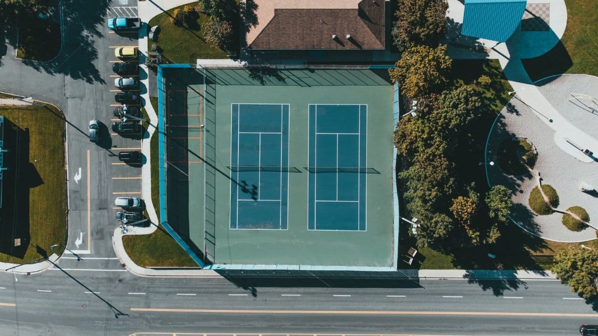 An aerial shot of tennis courts surrounded by urban infrastructure and green spaces.
