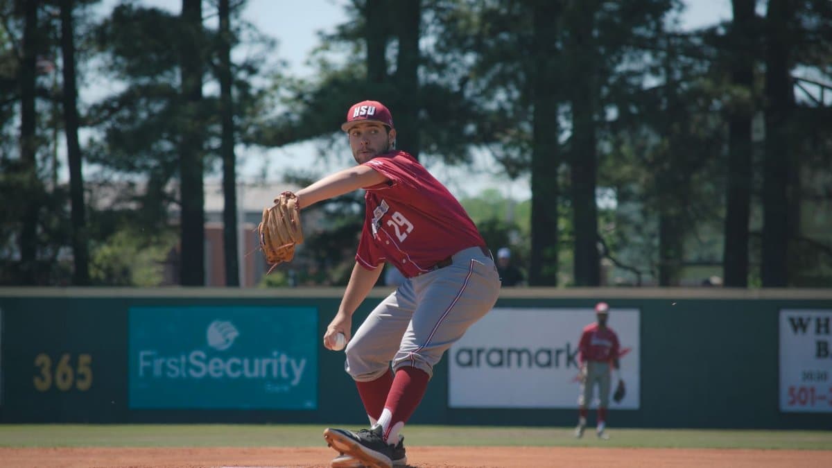 A focused baseball pitcher in red uniform prepares to throw on a sunny outdoor field.